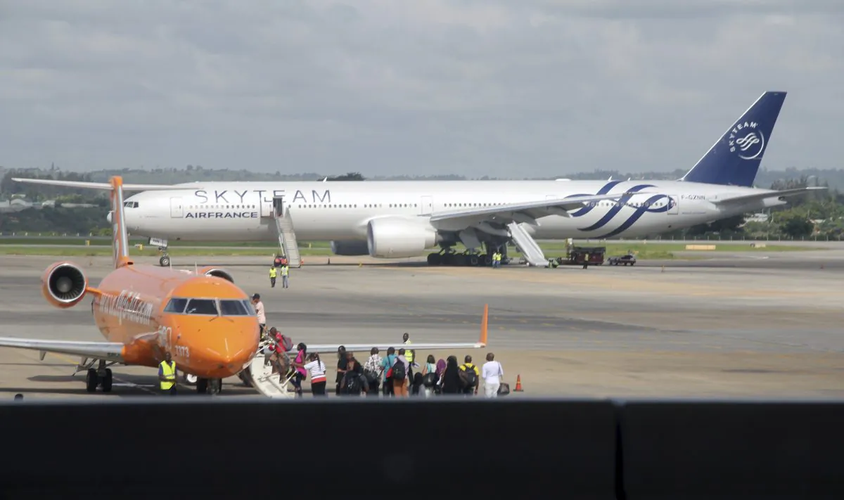 An Air France plane which made an emergency landing is seen behind passengers boarding on a small jetliner at Moi International Airport in Mombasa, Kenya, on Dec. 20, 2015. The Boeing 777 Air France flight 463 from Mauritius to Paris was forced to land in the Kenyan coastal city of Mombasa after a device suspected to be a bomb was found in the lavatory, a Kenyan police official said Sunday. The passengers shown in this photo are not the Air France plane evacuees. (AP Photo/Edwin Kana)
