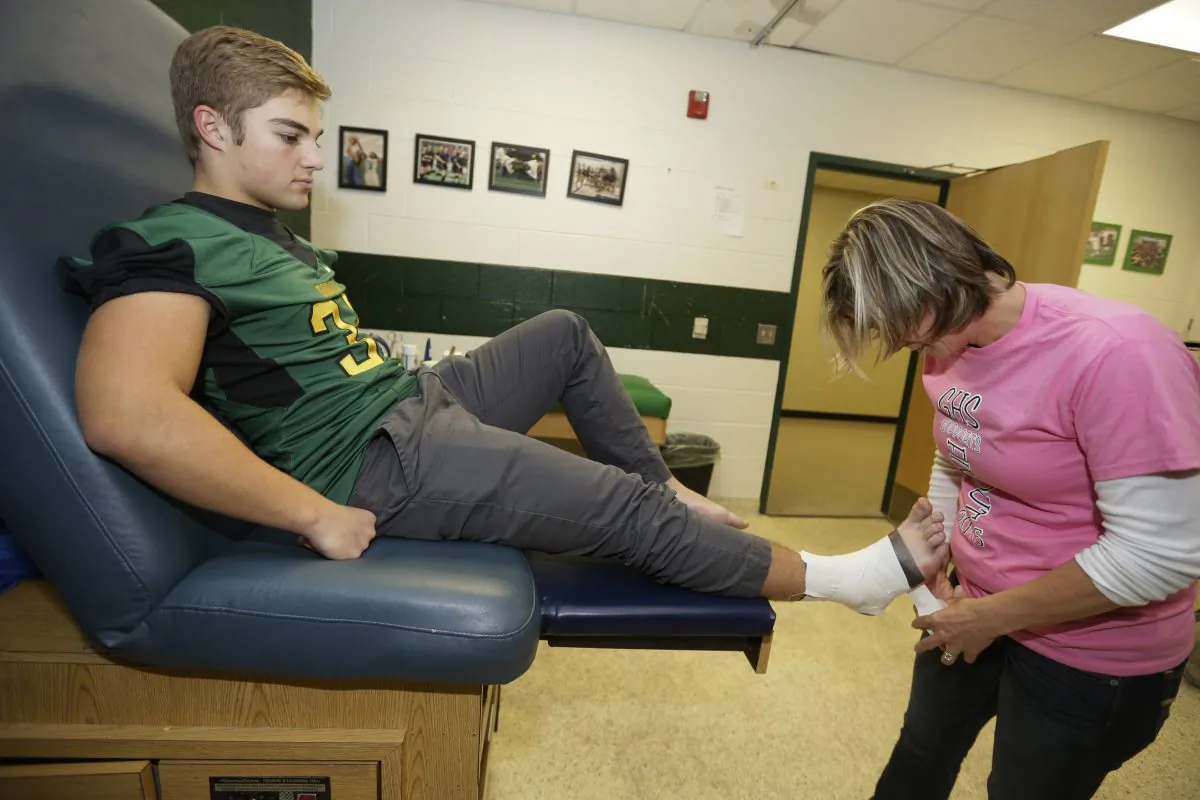 In this Oct. 23, 2015, photo, Birmingham Groves athletic trainer Kelly Salter, right, tapes linebacker Ian Rice before a football game in Beverly Hills, Mich. Last fall, Rice suffered a concussion that was so severe it sent him to the emergency room. His story is one that plays out for thousands of athletes on high school teams across the country. What's different is Groves is one of 62 Michigan high schools participating in a unique pilot concussion program that does baseline testing of athletes in football and other sports. (AP Photo/Carlos Osorio)
