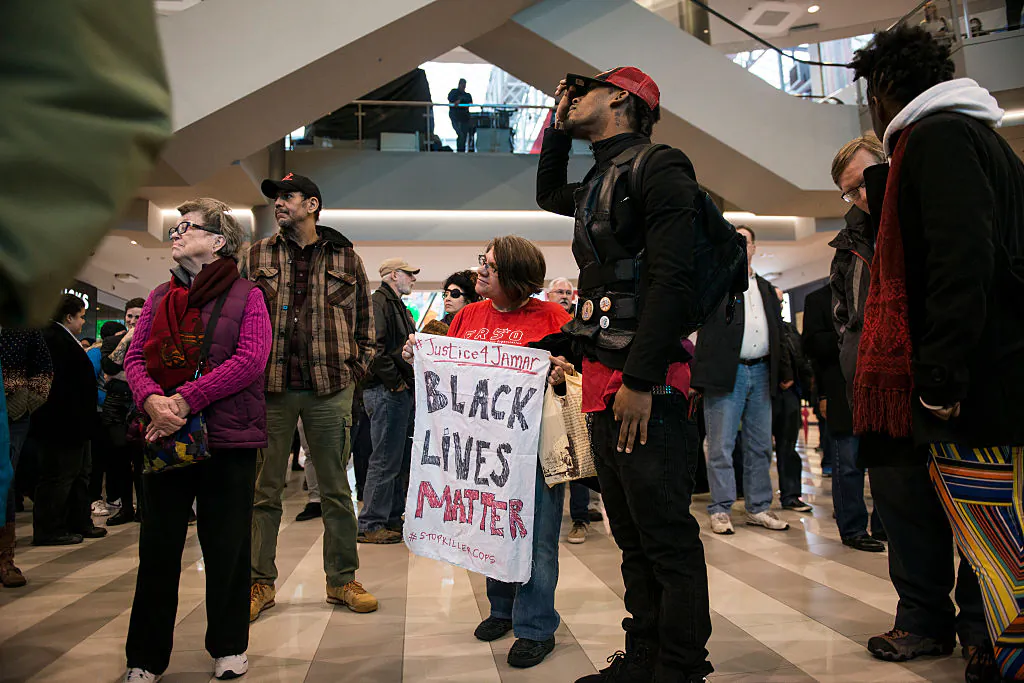 Activist, Jess Sundin, holds a sign that reads, 'BLACK LIVES MATTER,' in the rotunda of the Mall of America on December 23, 2015 in Bloomington, Minnesota. To Sundin's right stands Alexander Clark, cousin of Jamar Clark who was shot and killed by Minneapolis Police in November. Black Lives Matter Minneapolis staged a brief protest at the Mall of America in Bloomington, MN before moving their protest to the airport. (Photo by Stephen Maturen/Getty Images)