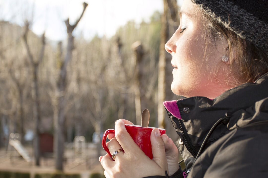 Beautiful woman holding a red mug with coffee at the sunrise