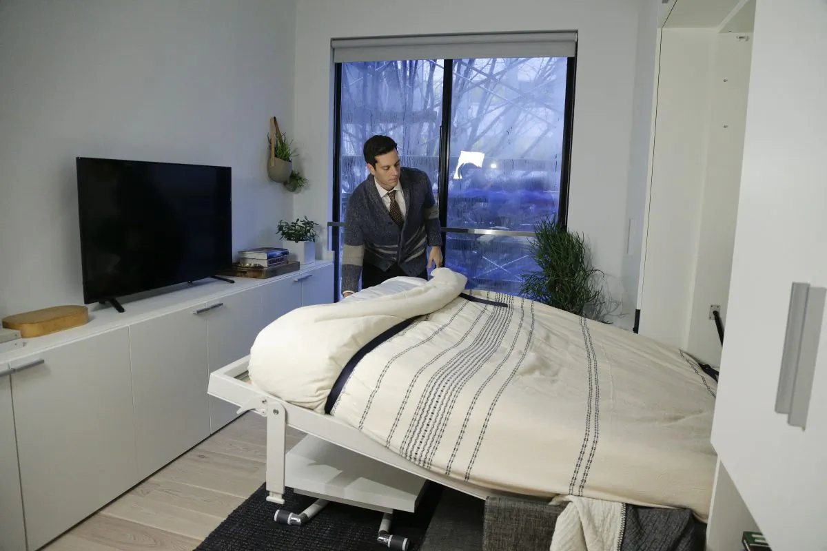 In this Dec. 22, 2015 photo, Stage 3 Properties co-founder Christopher Bledsoe demonstrates a retractable bed that turns into a sofa when stored inside one of the apartment units at the Carmel Place building in New York. As the city-sponsored micro-apartment project nears completion, its setting an example for tiny dwellings that the nations biggest city sees as an aid to easing its affordable housing crunch. (AP Photo/Julie Jacobson)