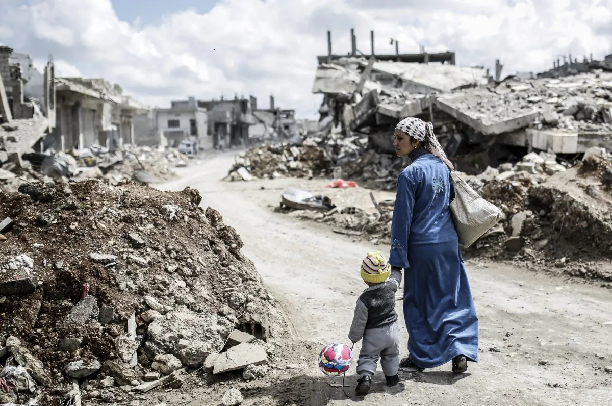 A Kurdish Syrian woman walks with her child past the ruins of the town of Kobani, also known as Ain al-Arab, on March 25, 2015. (Yasin Akgul/AFP/Getty Images)