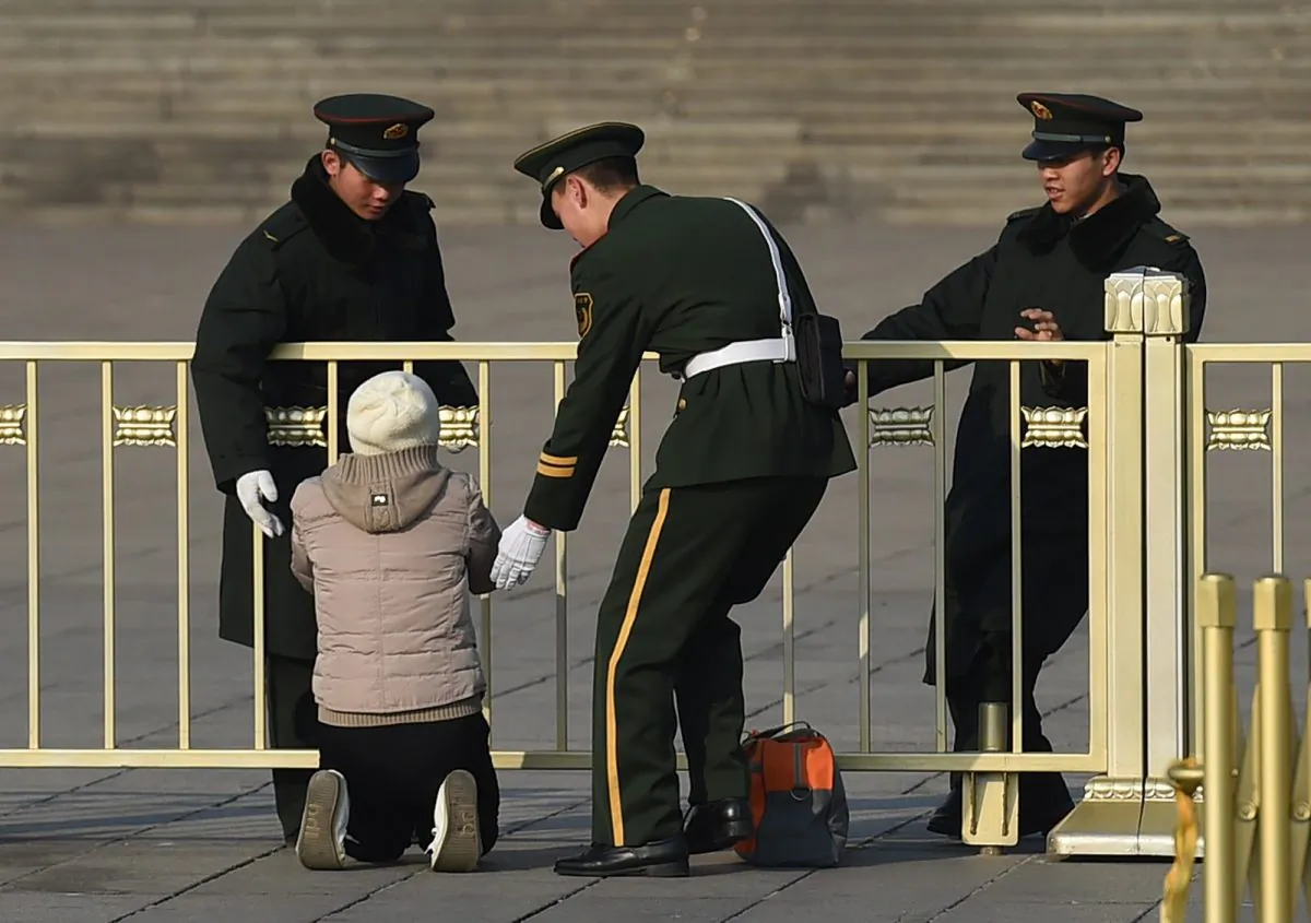 Paramilitary police officers stop a woman as she protests on her knees in front of the Great Hall of the People in Beijing on March 13, 2015.  (GREG BAKER/AFP/Getty Images)
