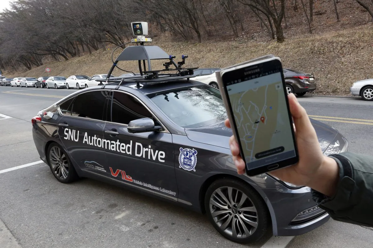 A researcher fromm the Intelligent Vehicle IT Research Center at Seoul National University shows the smartphone application for the driverless car called Snuber with a fixture on its roof with devices that scan road conditions at Seoul National University's campus in Seoul, South Korea, Tuesday, Jan. 5, 2016. (AP Photo/Lee Jin-man)