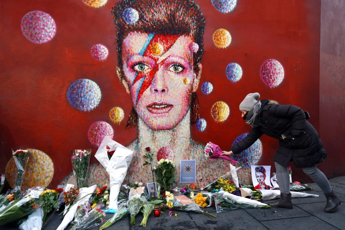 A woman leaves flowers beneath a mural of David Bowie in London on January 11, 2016. British music and fashion icon David Bowie died at the age of 69 after a battle with cancer. (Photo by Carl Court/Getty Images)