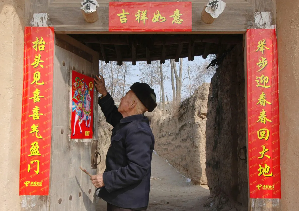 An elderly man pastes spring couplets on his door at a village on in Fu County of Shaanxi Province on Feb. 7, 2005. (China Photos/Getty Image)