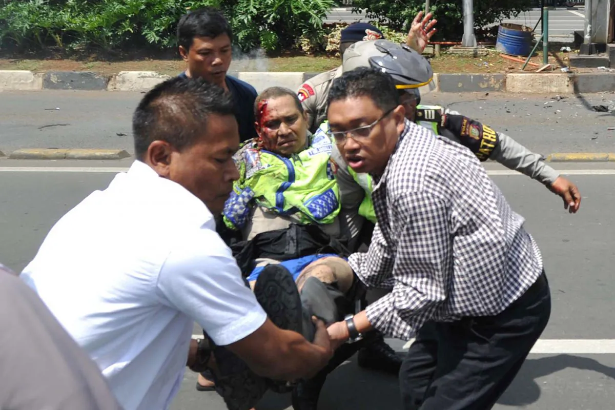 People carry an injured police officer near the site where an explosion went off at a police post, rear, in Jakarta, Indonesia Thursday, Jan. 14, 2016. Attackers set off explosions at a Starbucks cafe in a bustling shopping area in Indonesia's capital and waged gunbattles with police Thursday, leaving bodies in the streets as office workers watched in terror from high-rise windows. (AP Photo)
