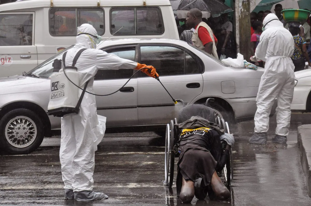 FILE - This is a Tuesday, Sept. 2, 2014 file photo of health workers as they spray the body of a amputee suspected of dying from the Ebola virus with disinfectant, in a busy street in Monrovia, Liberia, Tuesday, Sept. 2, 2014. (AP Photo/Abbas Dulleh, File)
