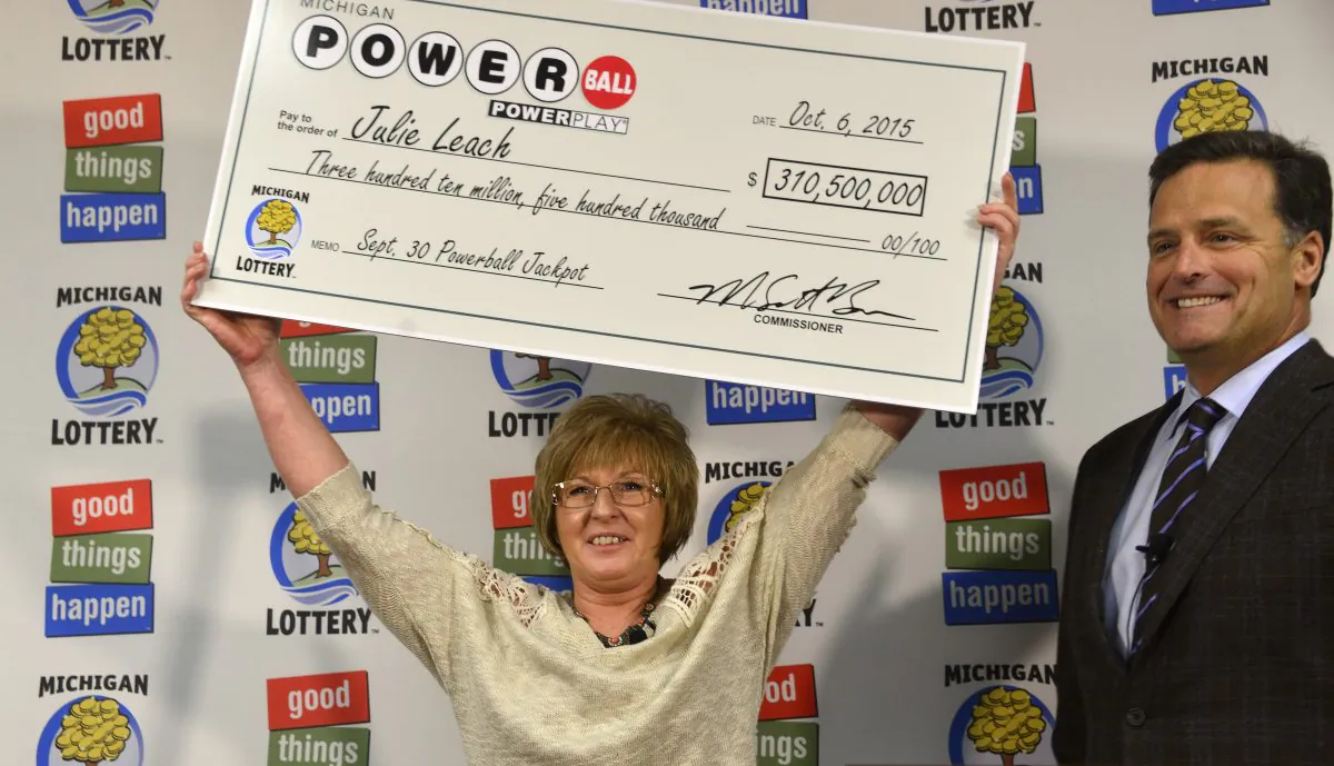 In this Oct. 6, 2015 file photo, Julie Leach of of Three Rivers, Mich., holds her $310 Million Powerball jackpot check, accompanied by Michigan Lottery Commissioner M. Scott Bowen in Lansing, Mich. (Dale G. Young/The Detroit News via AP)