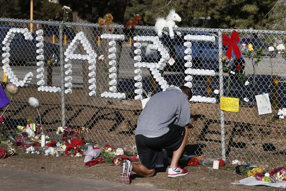 In this Dec. 16, 2013, file photo, Parker Semin, a 2011 Arapahoe High School graduate, prays at a makeshift memorial bearing the name of student Claire Davis, who was shot by Karl Pierson, a classmate during school three days earlier in an attack, in front of Arapahoe High School in Centennial, Colo. Legislation to allow lawsuits against Colorado schools for cases of violence  was signed into law Wednesday, June 3, 2015, by Gov. John Hickenlooper. (AP Photo/Brennan Linsley, File)