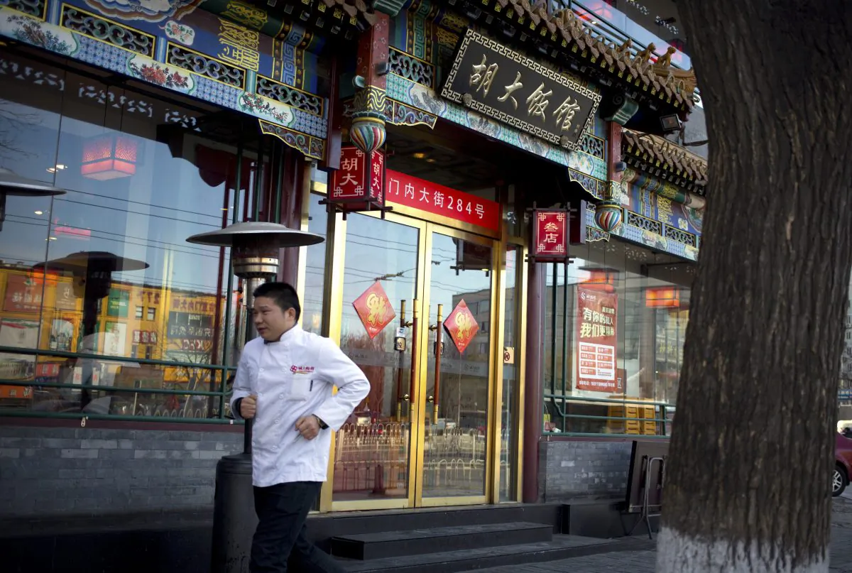 A man in a chef's uniform jogs past a branch of the Hu Da hot pot restaurant chain in Beijing on Jan. 22, 2016. (AP Photo/Mark Schiefelbein)