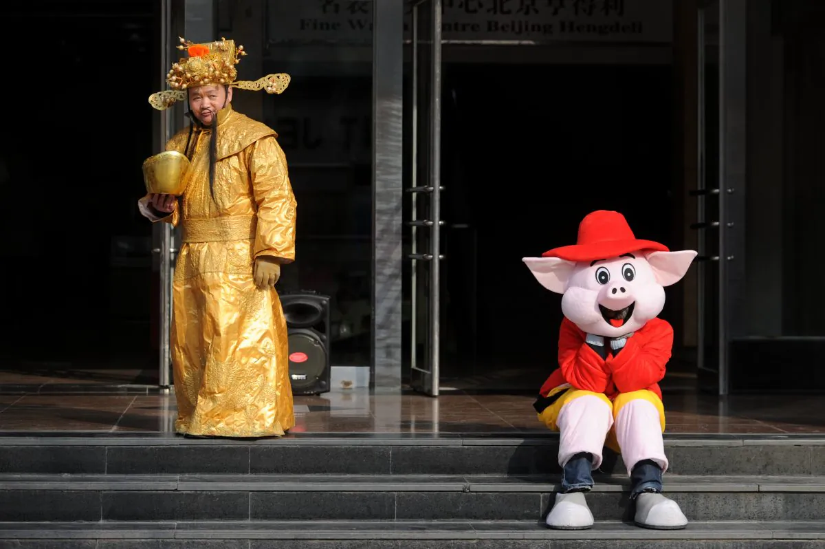 A sales man (L), dressed as the god of wealth, waits for customers with his partner (R) dressed as a cartoon character at the entrance of a shop in Beijing on March 22, 2013. (Wang Zhao/AFP/Getty Images)