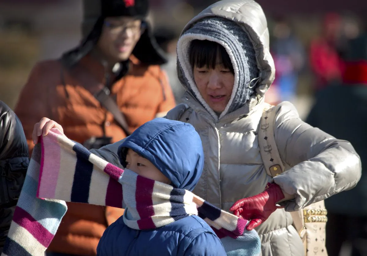 A woman ties a scarf around a boy's face in front of Tiananmen Gate near Tiananmen Square in Beijing, Saturday, Jan. 23, 2016. (AP Photo/Mark Schiefelbein)