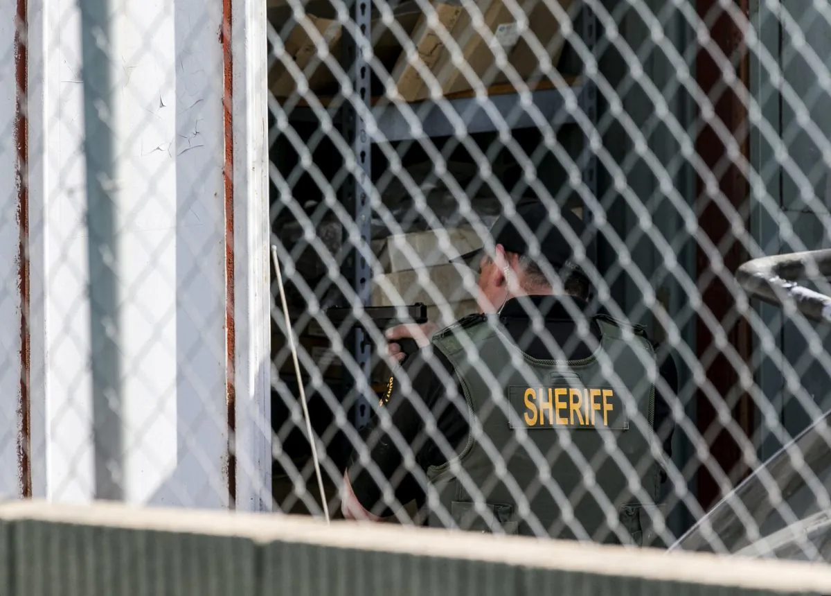 A Orange County Law enforcement agent points his gun inside a container while conducting a search for additional suspects at the back of an auto electric shop garage in Santa Ana, Calif., on Friday, Jan. 29, 2016.  (AP Photo/Damian Dovarganes)