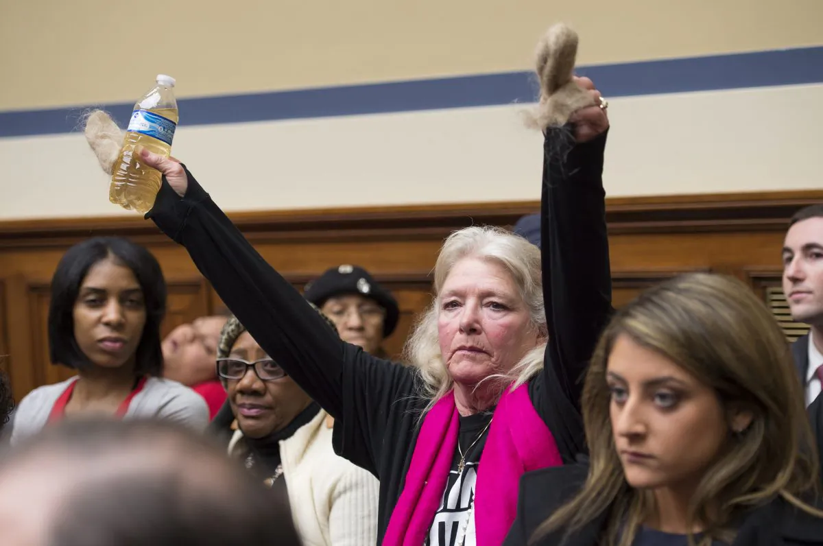 Flint, Mich. resident Glaydes Williamson holds up water from Flint and hair pulled from her drain, during the House Oversight and Government Reform Committee hearing to examine the ongoing situation in Flint, Mich., on Capitol Hill in Washington, D.C., on Feb. 3, 2016. Michigan should have required the city of Flint to treat its water for corrosion-causing elements after elevated lead levels were first discovered in the city's water a year ago, the state's top environmental regulator says in testimony prepared for congressional hearing. (AP Photo/Molly Riley)