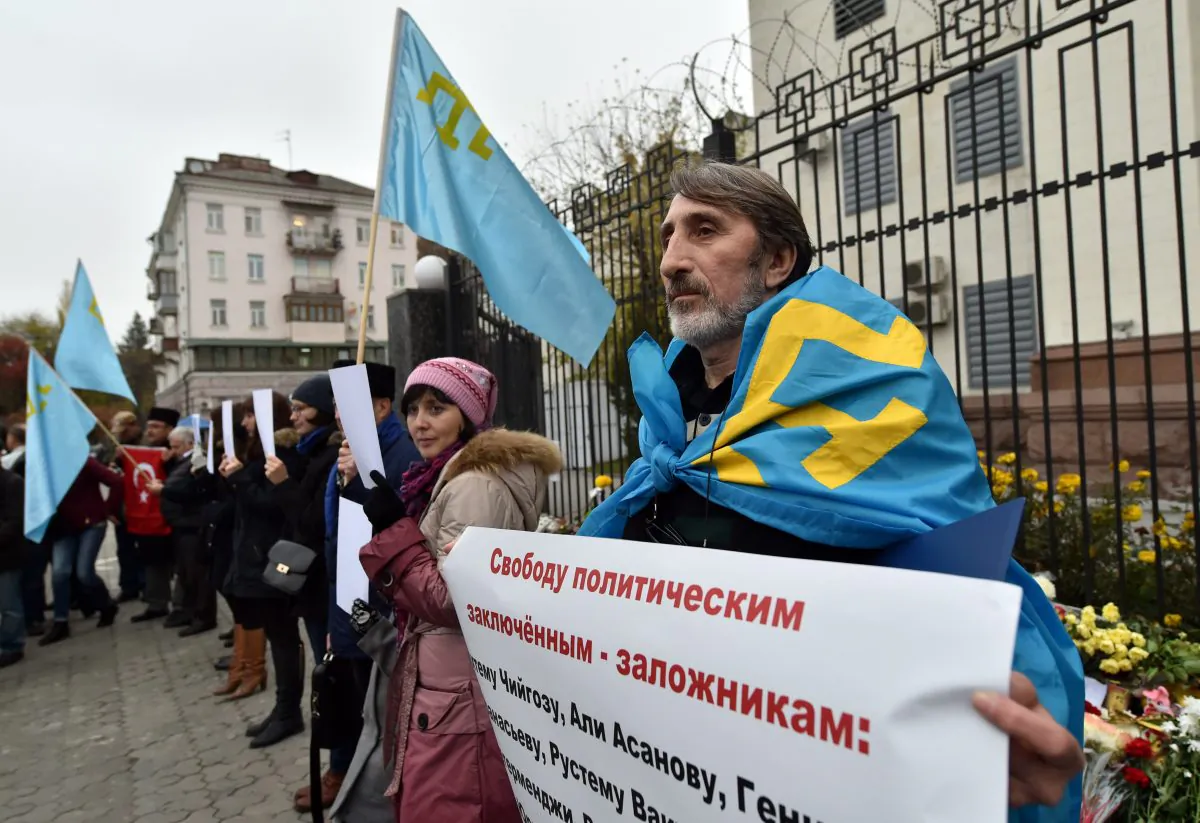 A Crimean Tatar covered with the flag of the Crimean Tatars, holds a placard reading "Free political prisoners-hostages".    (SERGEI SUPINSKY/AFP/Getty Images)