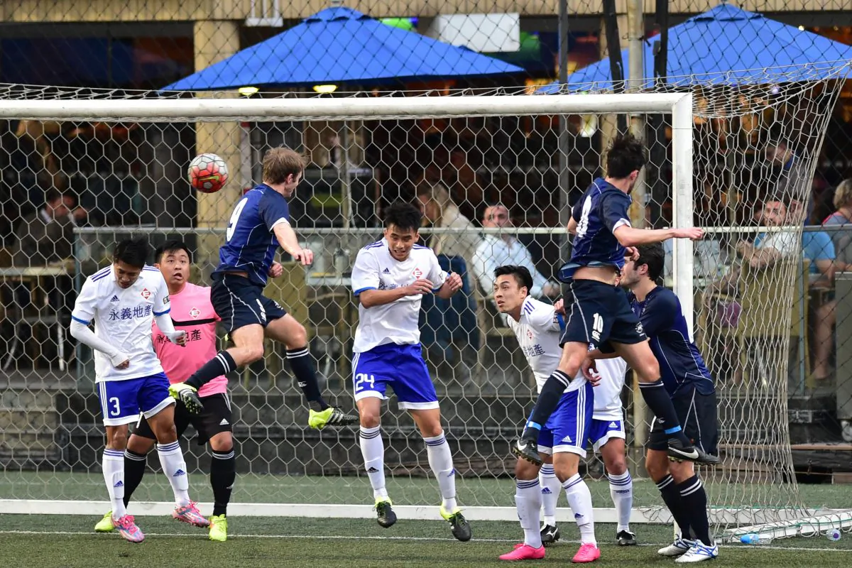 HKFC's Robbie Bacon (blue 9) has a header cleared by the Easyknit Property defence during HKFC's 4-1 victory in the division 1 of the HKFA League, at Sports Road on Sunday Feb 14. (Bill Cox/Epoch Times)