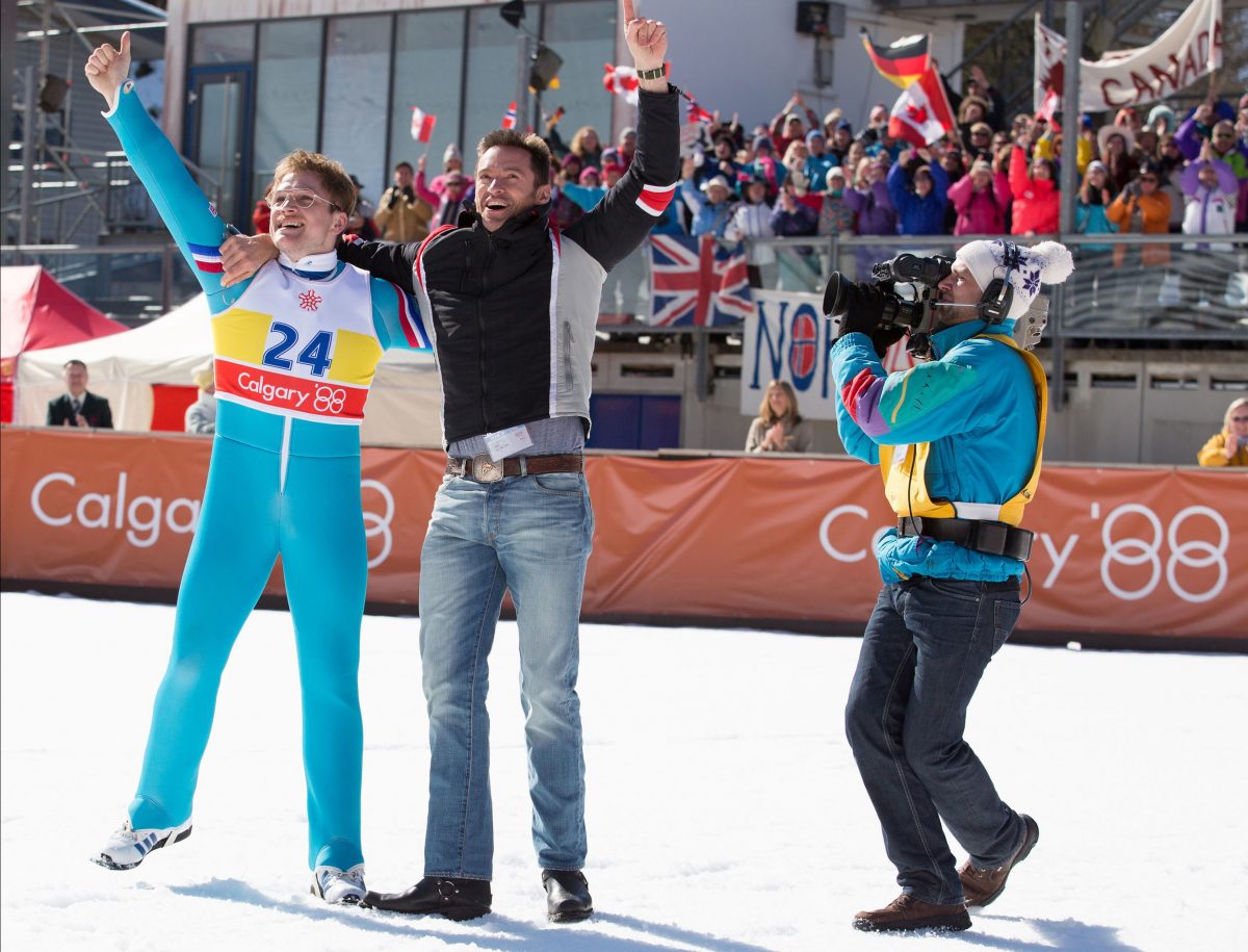 two men rejoice after winning skijump competition in "Eddie the Eagle"