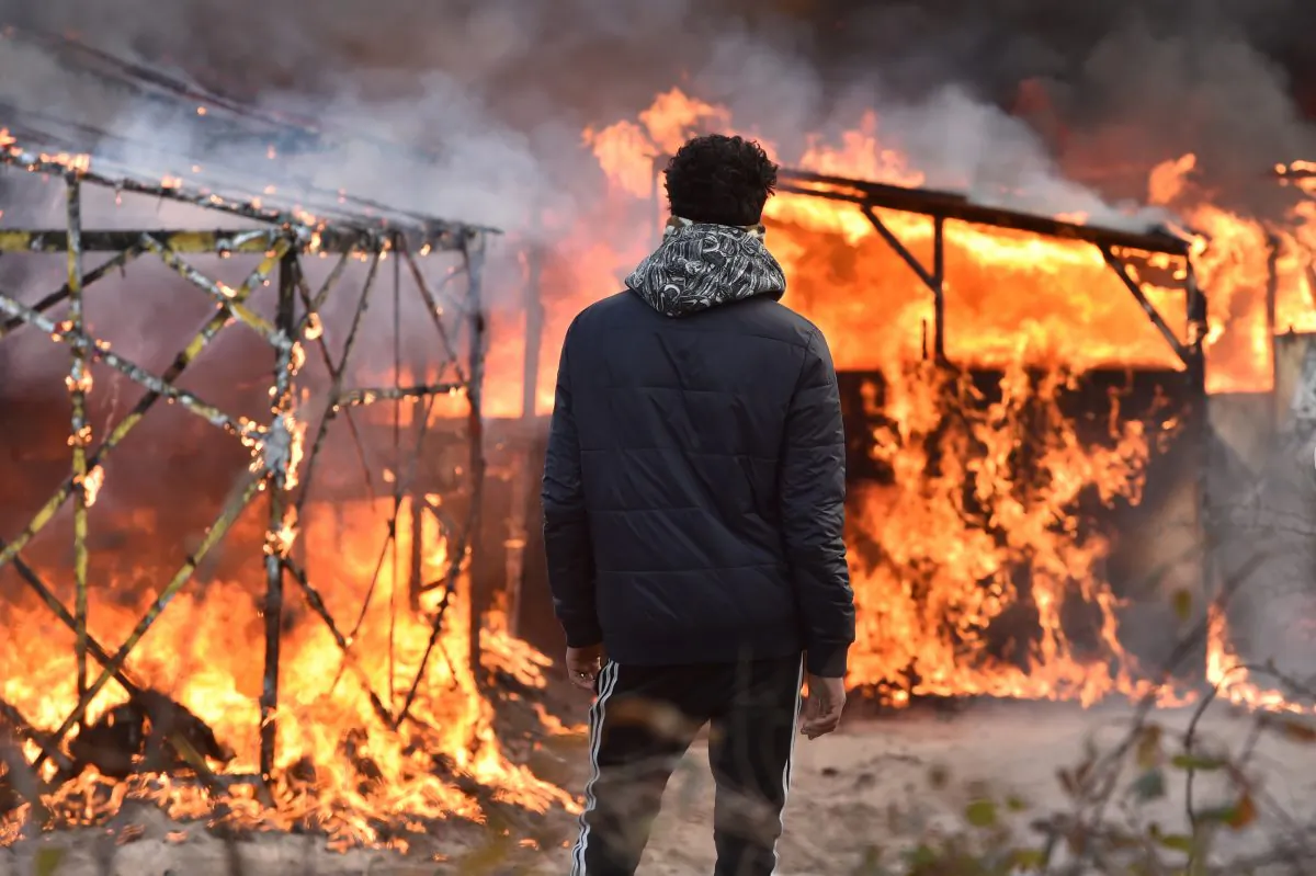 A migrant looks at shacks burning during the dismantling of half of the "Jungle" migrant camp in the French northern port city of Calais, on February 29, 2016. Clashes broke out between French riot police and migrants on February 29 as bulldozers moved into the grim shantytown on the edge of Calais known as the "Jungle" to start destroying hundreds of makeshift shelters. AFP PHOTO / PHILIPPE HUGUEN / AFP / PHILIPPE HUGUEN        (Photo credit should read PHILIPPE HUGUEN/AFP/Getty Images)