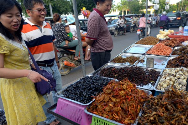 tourists smiling as they look at insects displayed for sale along a street in Phnom Penh. (Tang Chhin Sothy/AFP/Getty Images)