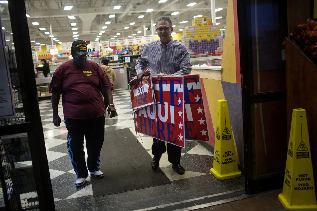 Volunteer election clerks Allie Green Jr., left,  and Paul Tryhus, right,  briefly leave a Fiesta Mart supermarket, a polling location, to place voting signs, before polls open in Austin, Texas on Tuesday, March 1, 2016. Republicans will vote in 11 states, with 595 delegates at stake. Democrats will vote in 11 states and American Samoa, with 865 delegates up for grabs. Some states have contests Tuesday for only one party.  (AP Photo/Tamir Kalifa)