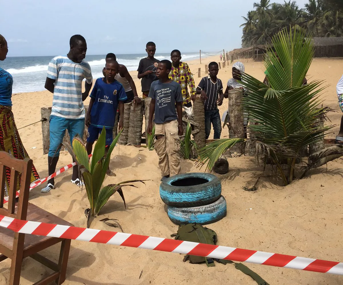 Local people stand near a taped off area that formed part of the crime scene outside the Nouvelle Paillote Hotel, one of the three hotels involved in an attack at Grand Bassam, Ivory Coast, Monday, March 14, 2016. Survivors of the first attack by Islamic extremists in Ivory Coast described scenes of confusion and fear as the jihadists gunned down defenseless civilians at a beachfront resort area. (AP Photo/Christin Roby)