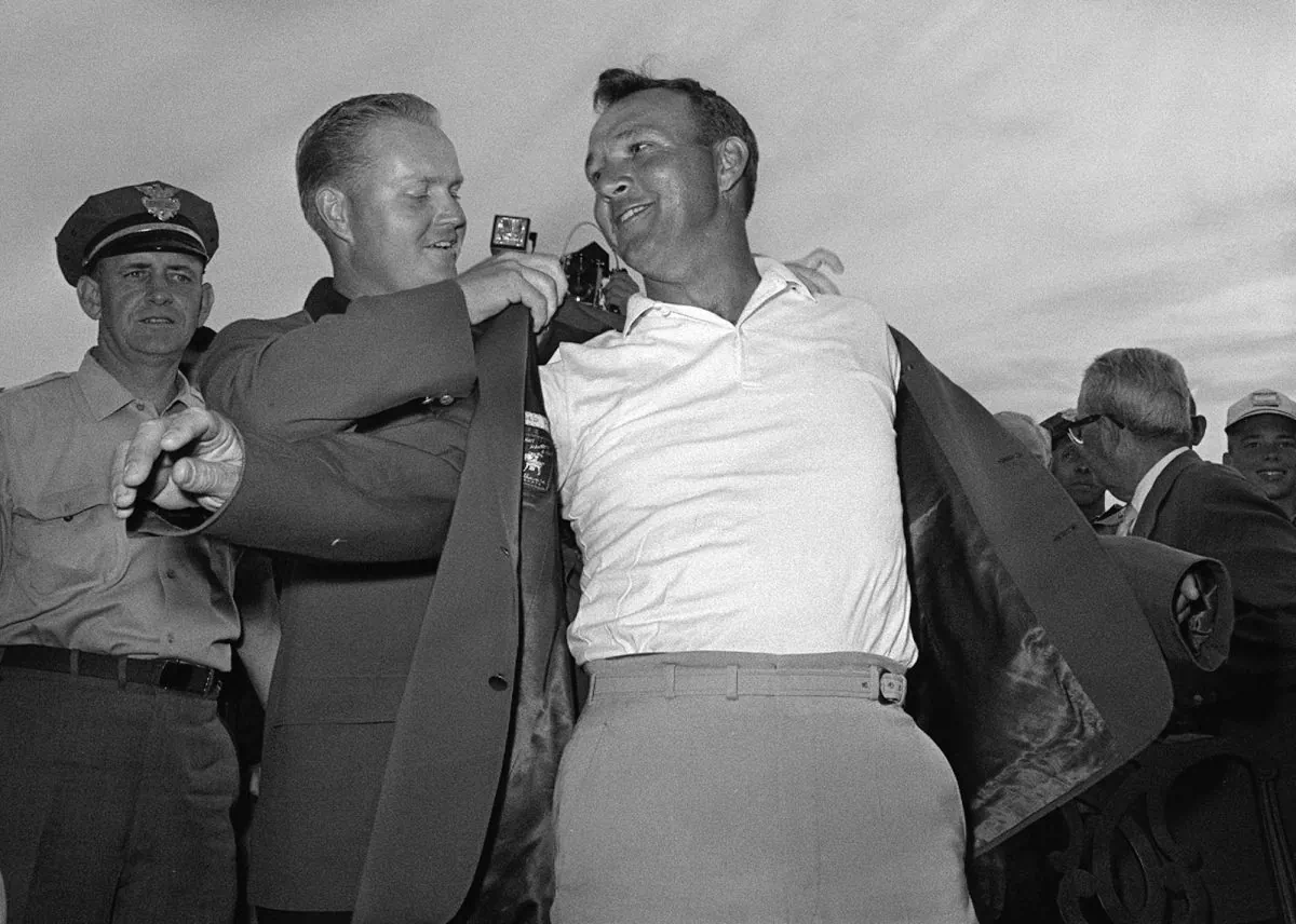 In this April 12, 1964 file photo, Arnold Palmer, right, slips into his green jacket with help from Jack Nicklaus after winning the Masters golf championship, in Augusta, Ga. Fifty years ago, Palmer won the Masters for the fourth time. It was his seventh major. He was 34, the King. (AP Photo/File)