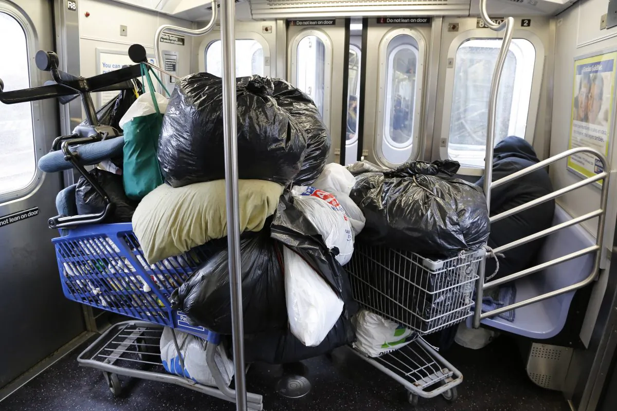 In this March 14, 2016 photo, a homeless man, right, sleeps with his belongings stacked into two shopping carts while riding the subway in New York. (AP Photo/Mark Lennihan)