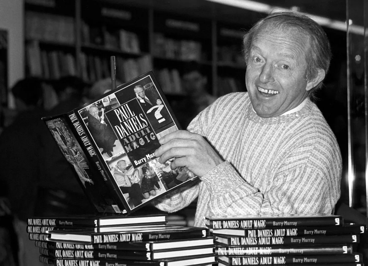 British magician Paul Daniels as he holds with a copy of his book "Adult Magic" at Whiteleys book shop in London on Dec. 2, 1989. Daniels, best known for The Paul Daniels Magic Show that regularly attracted 15 million TV viewers in Britain and was sold to 43 countries, has died after suffering from an inoperable brain tumor. He was 77. His publicist, Bex Colwell, said, in a statement that Daniels died Thursday, March 17, 2016, at his home in Berkshire, 60 miles west of London with his wife by his side. (PA via AP)