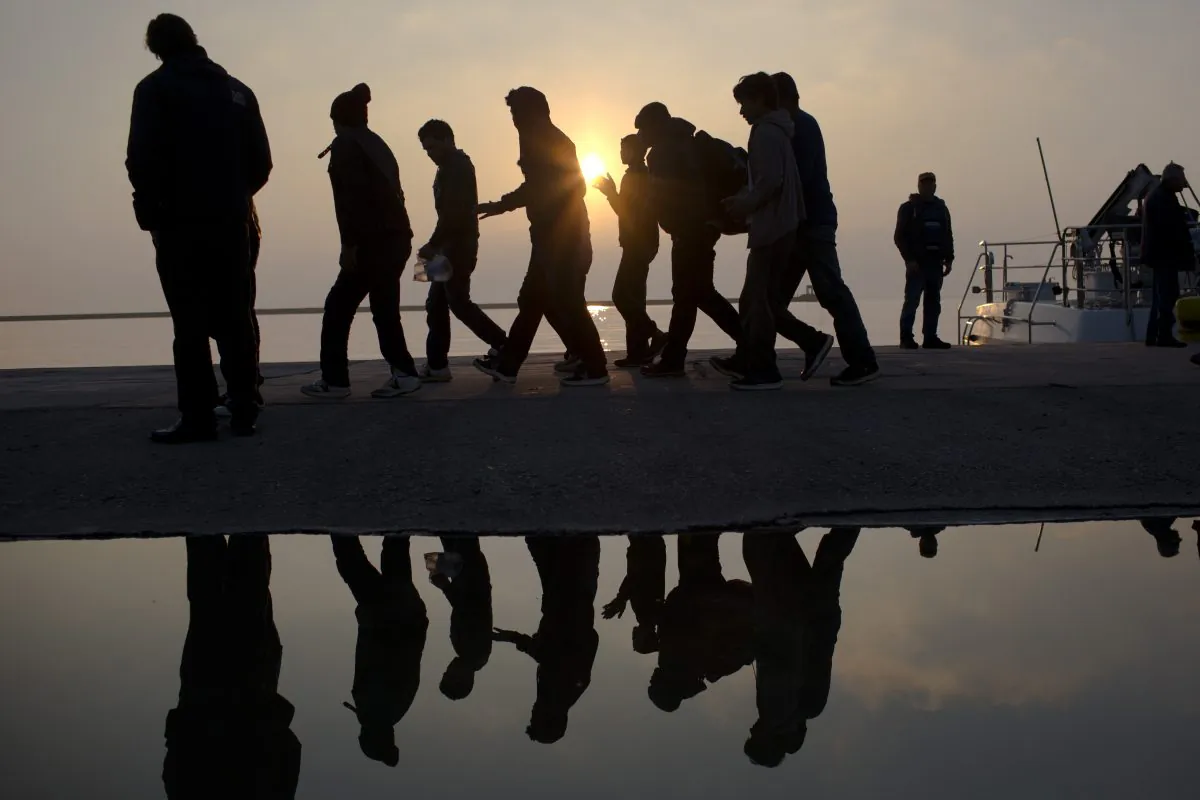 Migrants are reflected in a water puddle as they disembark off the coast of the Greek island of Lesbos on March 21, 2016. (Petros Giannakouris/AP Photo)