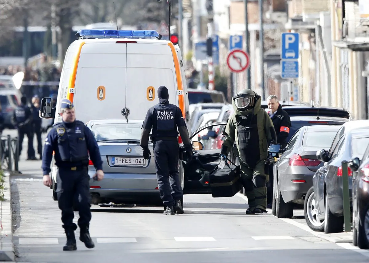 A member of emergency services wearing protective clothing, at right, investigates the scene in Schaerbeek, Belgium, Friday March 25, 2016. (AP Photo/Alastair Grant)