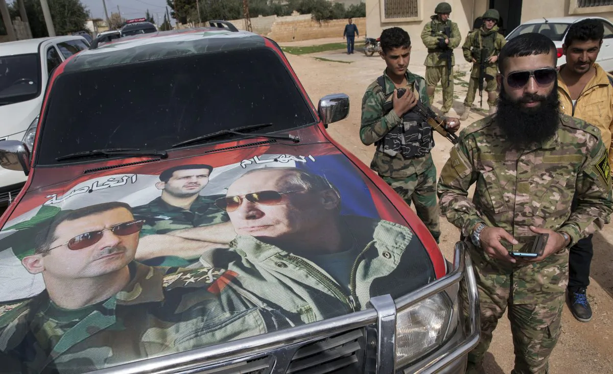 Syrian and Russian soldiers, who escort a group of journalists in the background, stand near a car covered by collage showing photos of faces of Russian President Vladimir Putin (R), Syrian President Bashar Assad (L), and a Syrian general, President's Assad brother, Maher Assad (C), in Maarzaf, about 10 miles west of Hama, on March 2, 2016. (Pavel Golovkin/AP Photo)
