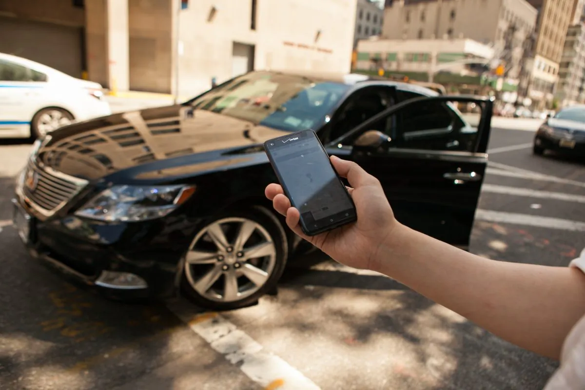 A person with a smartphone displaying the Uber app, before getting in a black Lexus which was hailed using the app, in Manhattan, on June 8, 2014. (Benjamin Chasteen/Epoch Times)