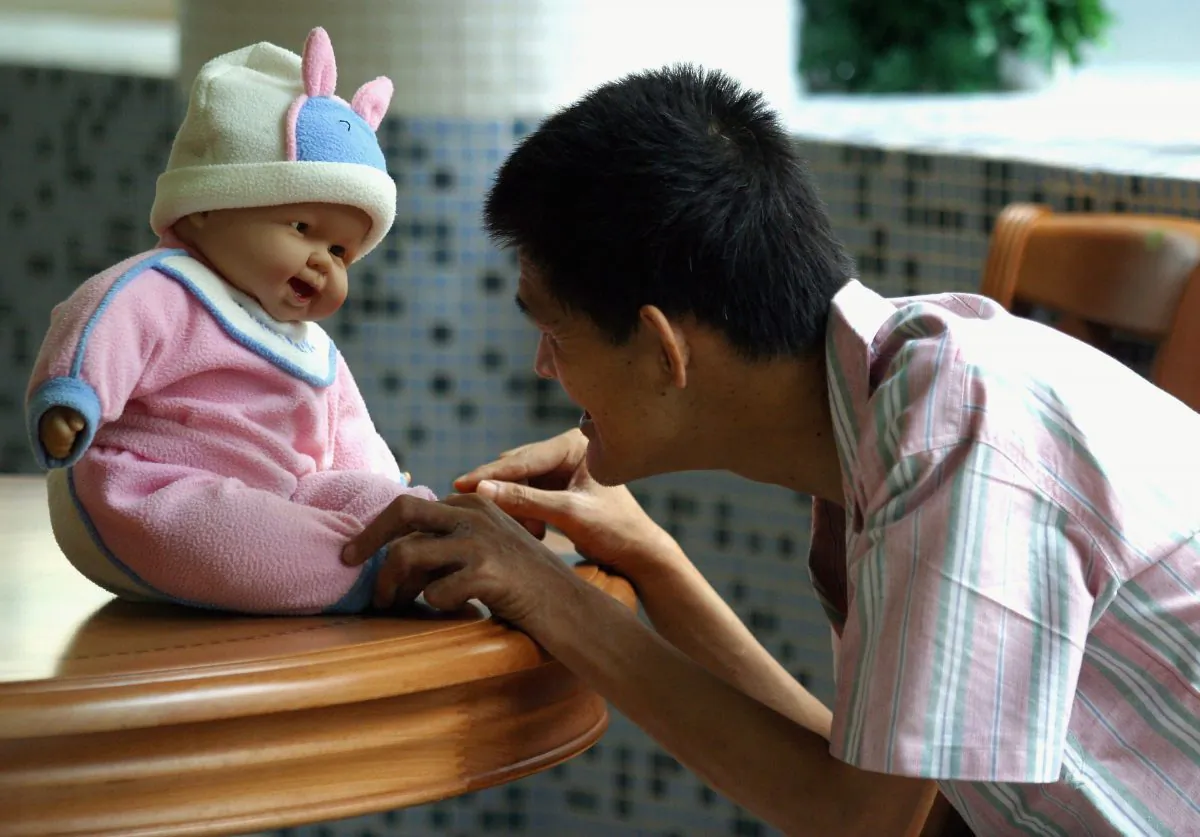 A man who suffers from senile dementia plays with a doll as a treatment to remind him of the old days at the Cihui Rehabilitation Center for the Aged in Guangzhou, Guangdong Province, China, on Sept. 2, 2005. (China Photos/Getty Images)