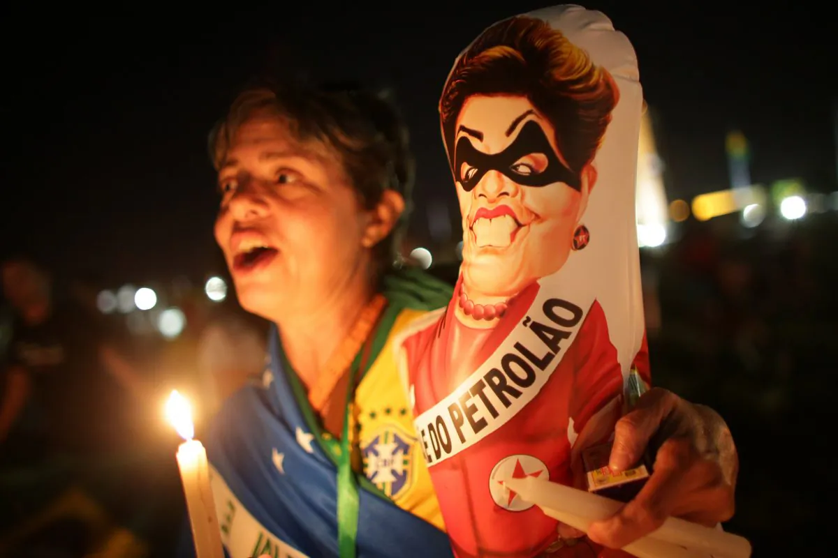 An Anti-government demonstrator holds a caricature of Brazil's President Dilma Rousseff wearing a bandit mask and sash that reads in Portuguese "Big oil" outside Congress where lawmakers debate whether to oust the Brazilian President Dilma Rousseff in Brasilia, Brazil, on April 16, 2016. Sunday's vote will determine whether the impeachment proceeds to the Senate. Rousseff is accused of violating Brazil's fiscal laws to shore up public support amid a flagging economy. (AP Photo/Eraldo Peres)