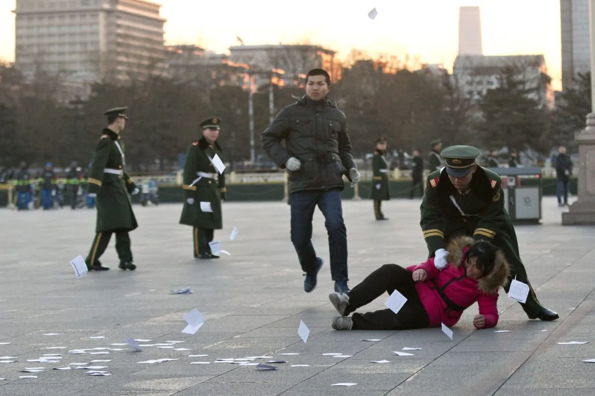 A petitioner is pushed on the ground by a paramilitary policeman after she ran into a cordoned off area near a national flag pole on Tiananmen Square and threw up flyers to protest her case of injustice, in Beijing, on March 5, 2014. (Alexander F. Yuan/AP Photo)
