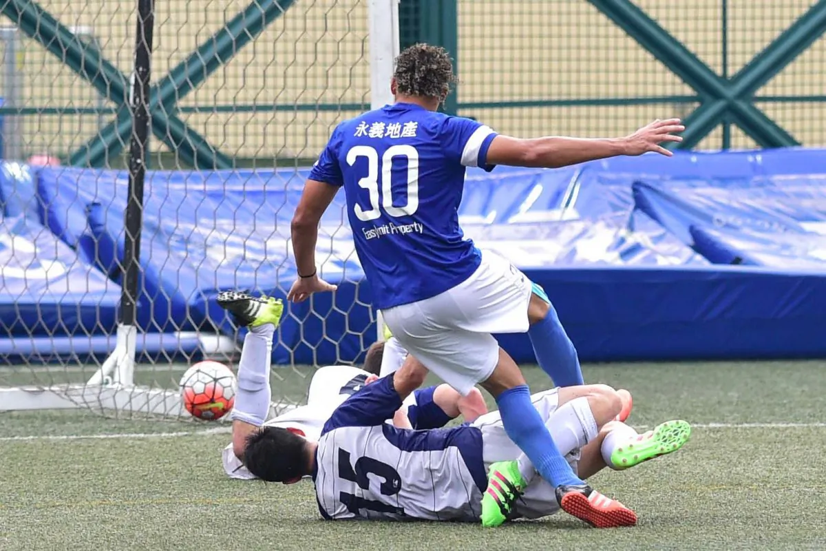 After slipping the ball past a charging Lucky Mile goalie, Beto Doc Santos, Jose Wellington of Easyknit Property, side foots the ball into the net while under pressure from two Lucky Mile defenders, increasing the lead of Easyknit Property to 4-2, the final score, in the HKFA First division match at Sports Road on Sunday May 1, 2016. (Bill Cox/Epoch Times)