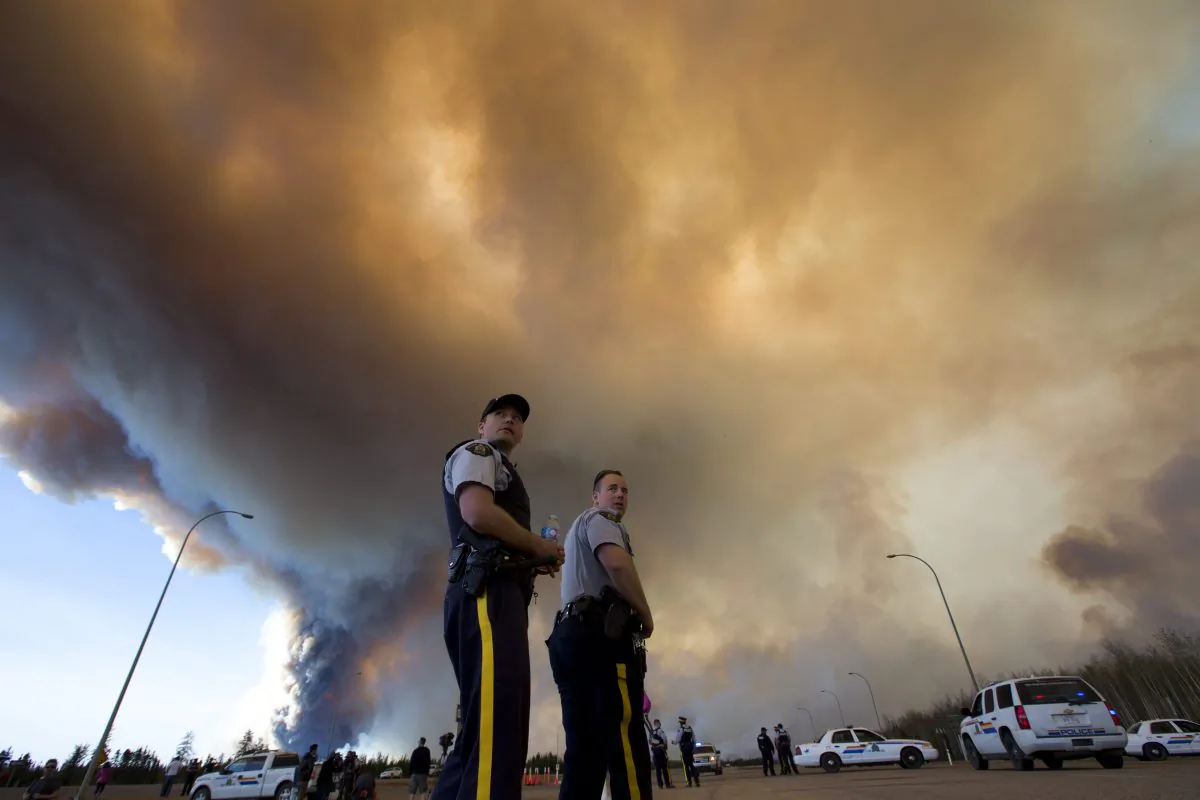 Police officers direct traffic under a cloud of smoke from a wildfire in Fort McMurray, Alberta, Canada on Friday, May 6, 2016. (Jason Franson/The Canadian Press via AP)