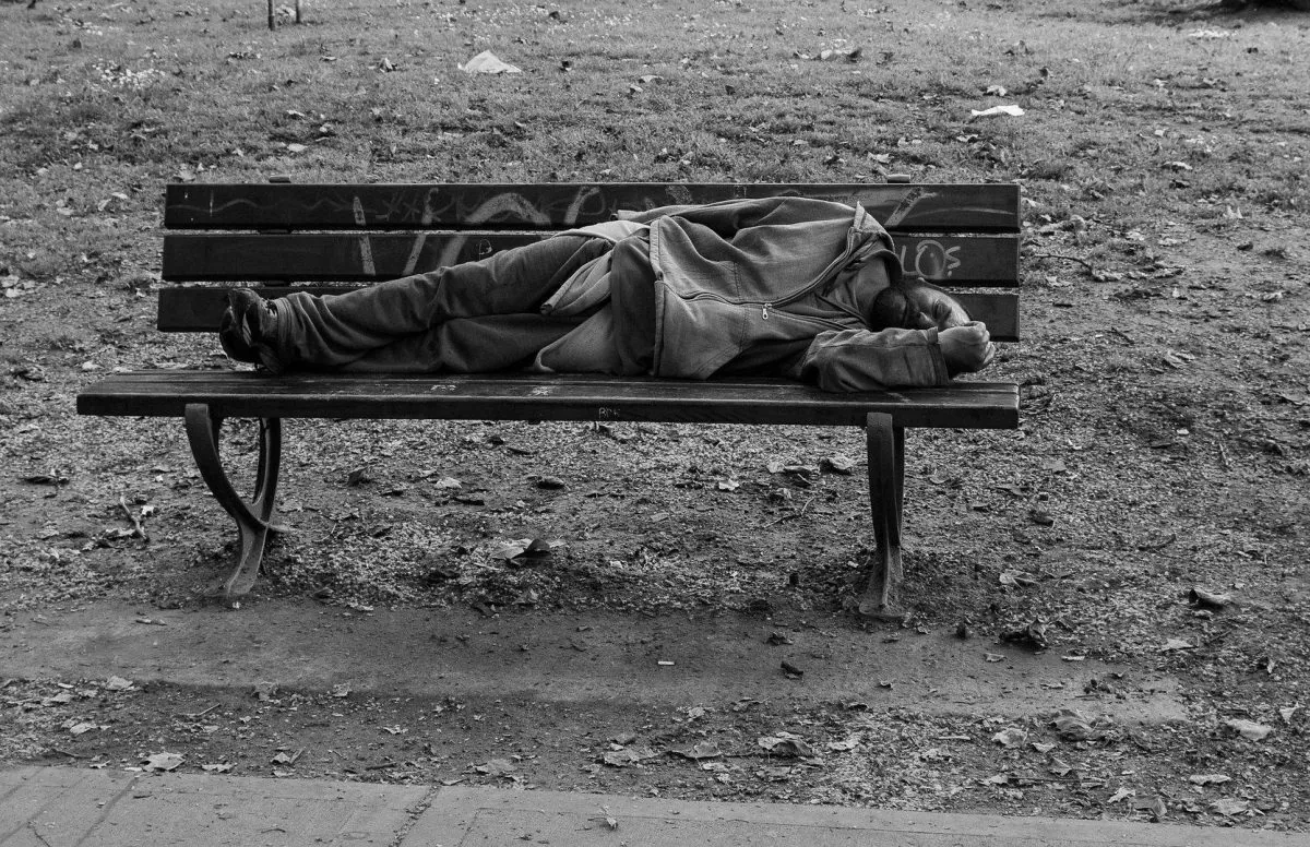 A homeless man sleeps on a park bench. (Public domain)