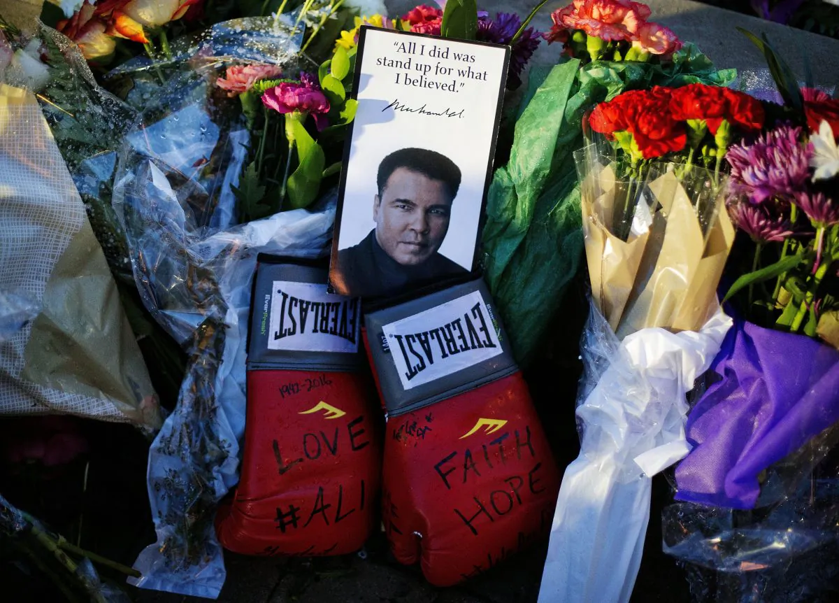Boxing gloves and a message sit among flowers at a makeshift memorial to Muhammad Ali at the Muhammad Ali Center in Louisville, Ky., on June 4, 2016. Muhammad Ali died Friday, June 3, at age 74. (AP Photo/David Goldman)