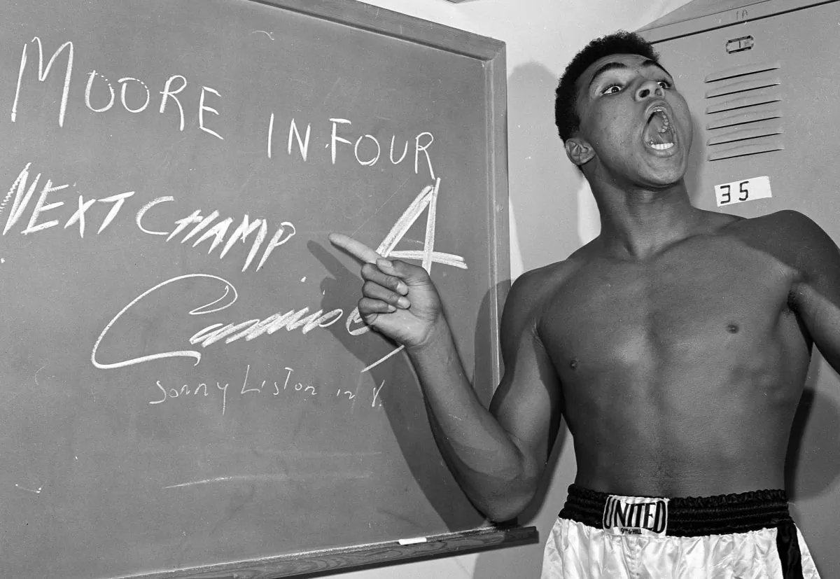 Cassius Clay points to a sign he wrote on a chalk board in his dressing room before his fight against Archie Moore in Los Angeles, on Nov. 15, 1962, predicting he'd knock Moore out in the fourth round, which he went on to do. (AP Photo/Harold P. Matosian)