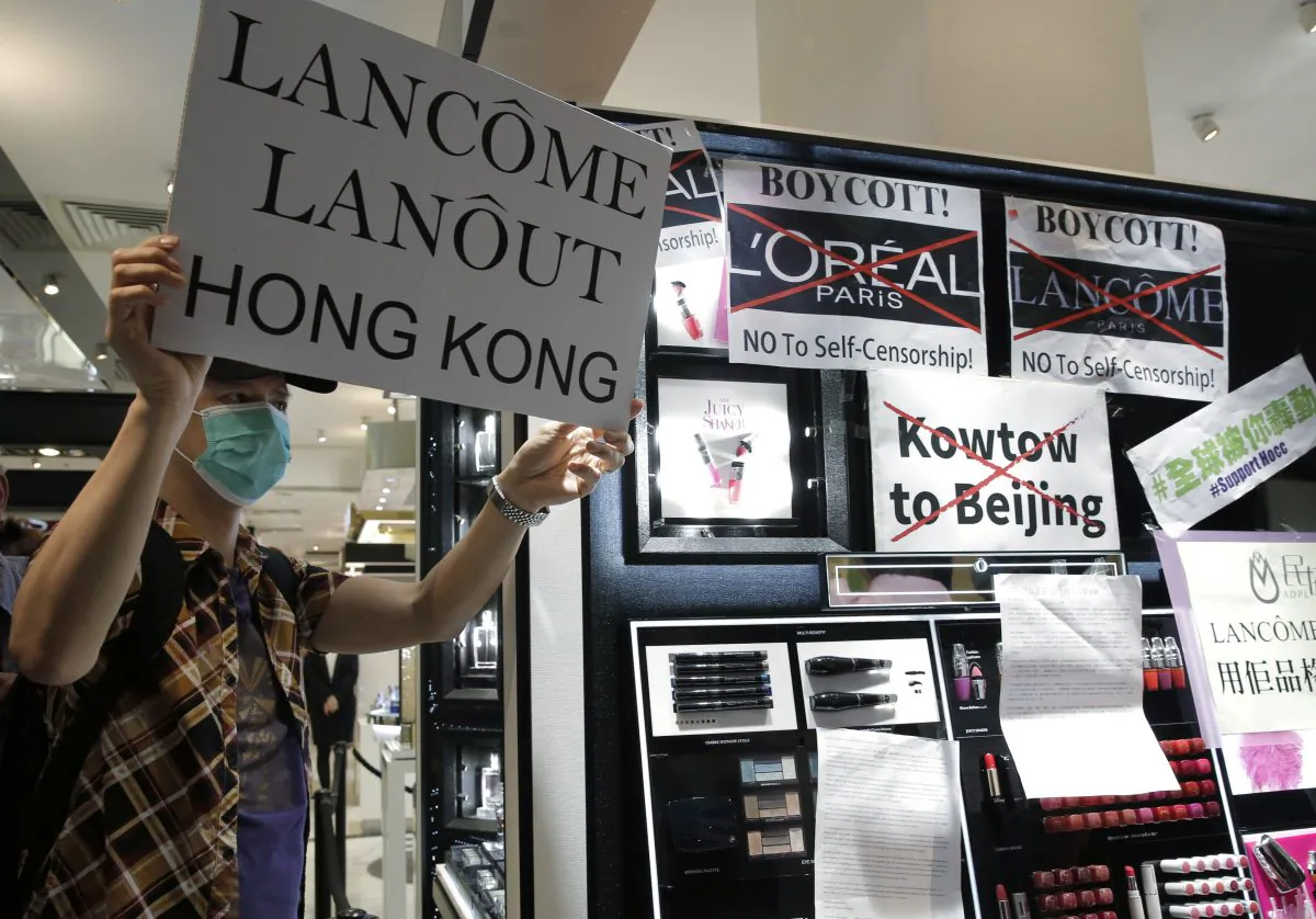 A protestor displays a placard at a Lancome counter inside a department store at Hong Kong's Times Square, Wednesday, June 8, 2016. French cosmetics company Lancome has sparked a backlash in Hong Kong after it canceled a promotional concert featuring a singer known for pro-democracy views, with many accusing it of caving in to political pressure from Beijing. (AP Photo/Kin Cheung)