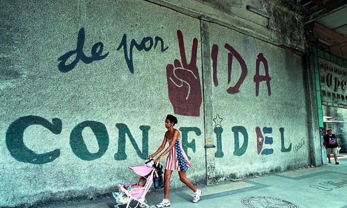 A woman dressed in the colors of the United States flag pushes her baby as they walk past a wall that reads, "A Lifetime with Fidel," June 11, 2001 in Havana, Cuba. (Jorge Rey/Getty Images)