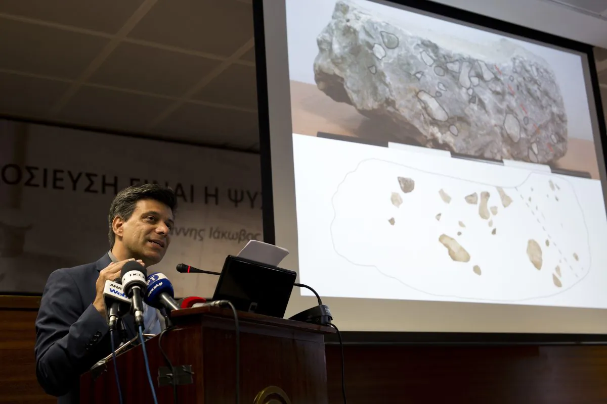 Greek archaeologist Christofilis Maggidis speaks as a photograph of a stone he believes belonged to the lost royal throne in the ancient palace of Mycenae, heart of the Mycenaean civilization, in southern Greece, during a press conference in Athens, on June 14, 2016. Maggidis says the worked stone, found by chance two years ago under the prehistoric citadel, is a chunk of the monolithic throne that was smashed when an earthquake sent part of the palace tumbling into a streambed below. (AP Photo/Petros Giannakouris)