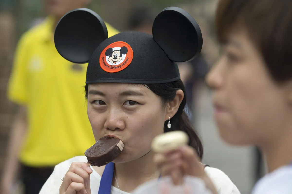 A visitor wearing a Mickey Mouse hat eats a Mickey Mouse-shaped ice cream during a tour on the eve of the opening of the Disney Resort in Shanghai, China, Wednesday, June 15, 2016. (AP Photo/Ng Han Guan)