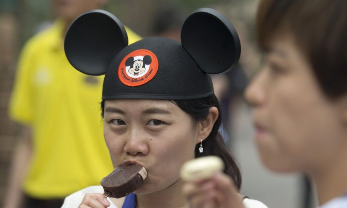 A visitor wearing a Mickey Mouse hat eats a Mickey Mouse-shaped ice cream during a tour on the eve of the opening of the Disney Resort in Shanghai, China, Wednesday, June 15, 2016.  (AP Photo/Ng Han Guan)