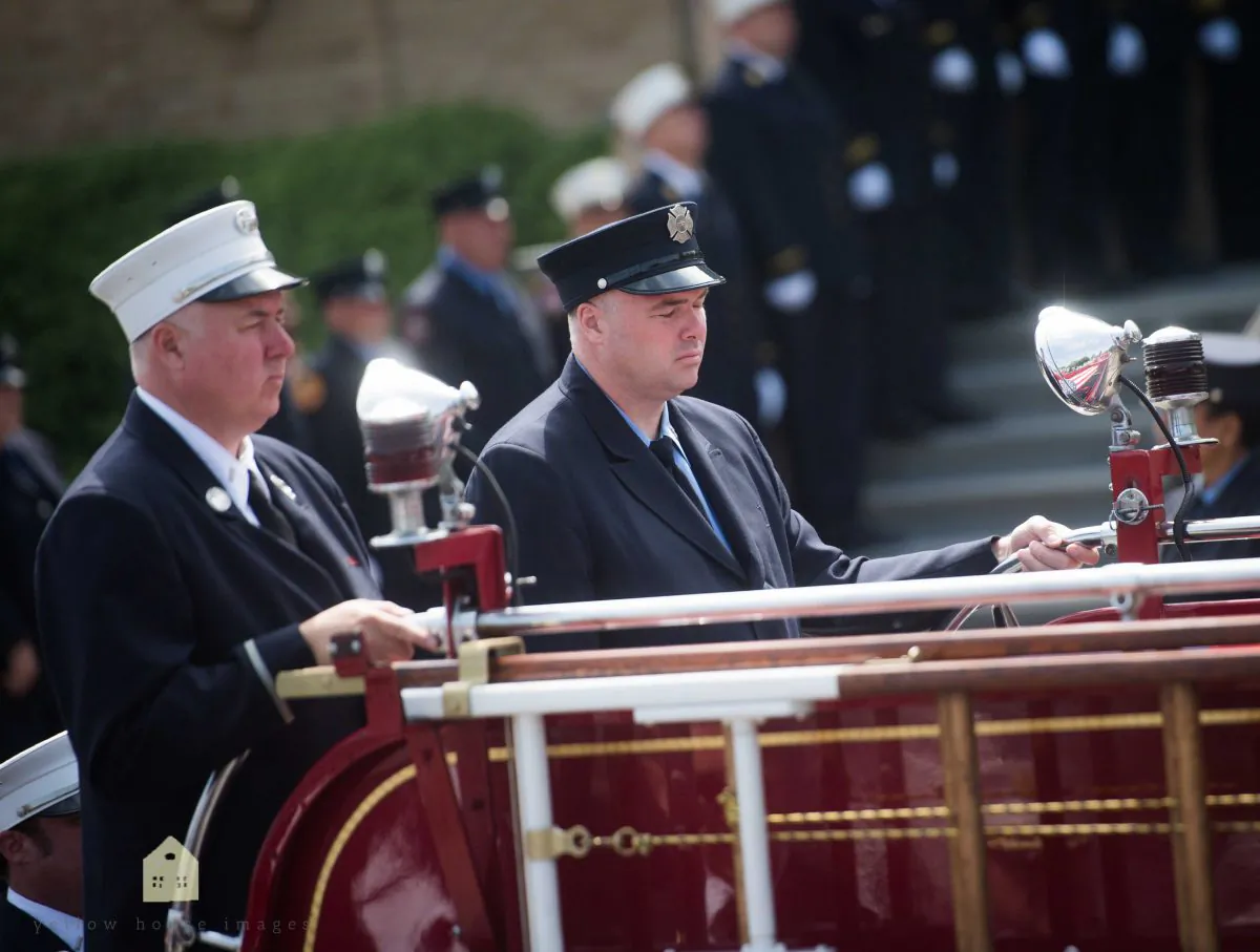 Firefighters Lt. Michael Stack (white hat) and Brian Stack (dark hat) ride on the back of the fire truck during the funeral of their father Fire Department of New York Battalion Chief Lawrence Stack who was killed in the World Trade Center terror attacks of September 11, 2001, outside Saints Philip and James Roman Catholic Church June 17, 2016 in St James, New York. (Andrew Theodorakis/Getty Images)
