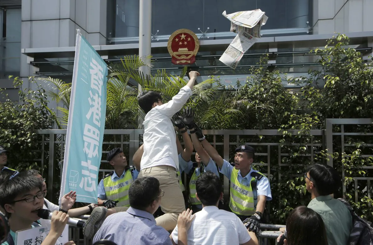 Oscar Lai, a member of pro-democracy group Demosisto, throws a newspaper reporting Hong Kong bookseller Lam Wing-Kee into the Chinese central government's liaison office in Hong Kong, Friday, June 17, 2016. Lam, one of the five Hong Kong booksellers whose disappearances sparked international concern, said Thursday he spent months confined in a room under constant surveillance by mainland Chinese authorities, who interrogated him about his publishing company's authors and customers. (AP Photo/Kin Cheung)