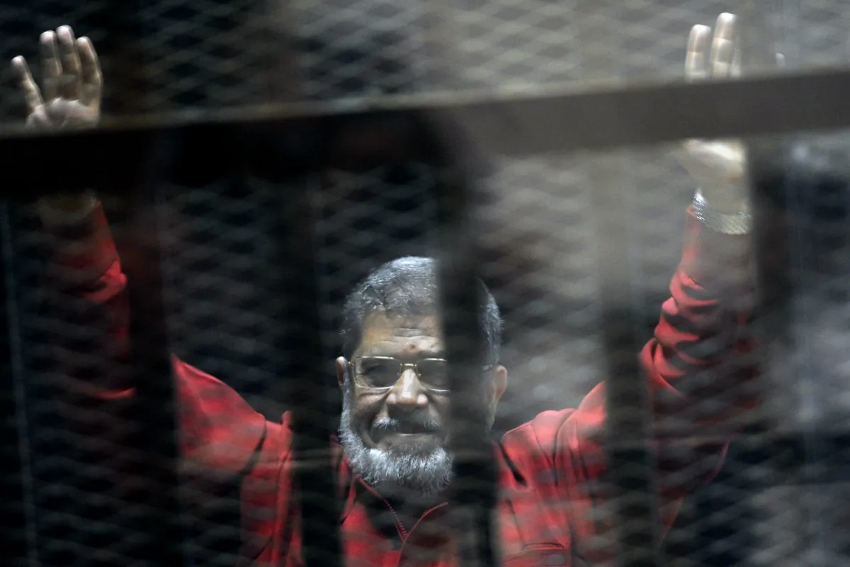 Former Egyptian President Mohammed Morsi, wearing a red jumpsuit that designates he has been sentenced to death, raises his hands inside a defendants cage in a makeshift courtroom at the national police academy, in an eastern suburb of Cairo, Egypt, on June 21, 2015. (AP Photo/Ahmed Omar)