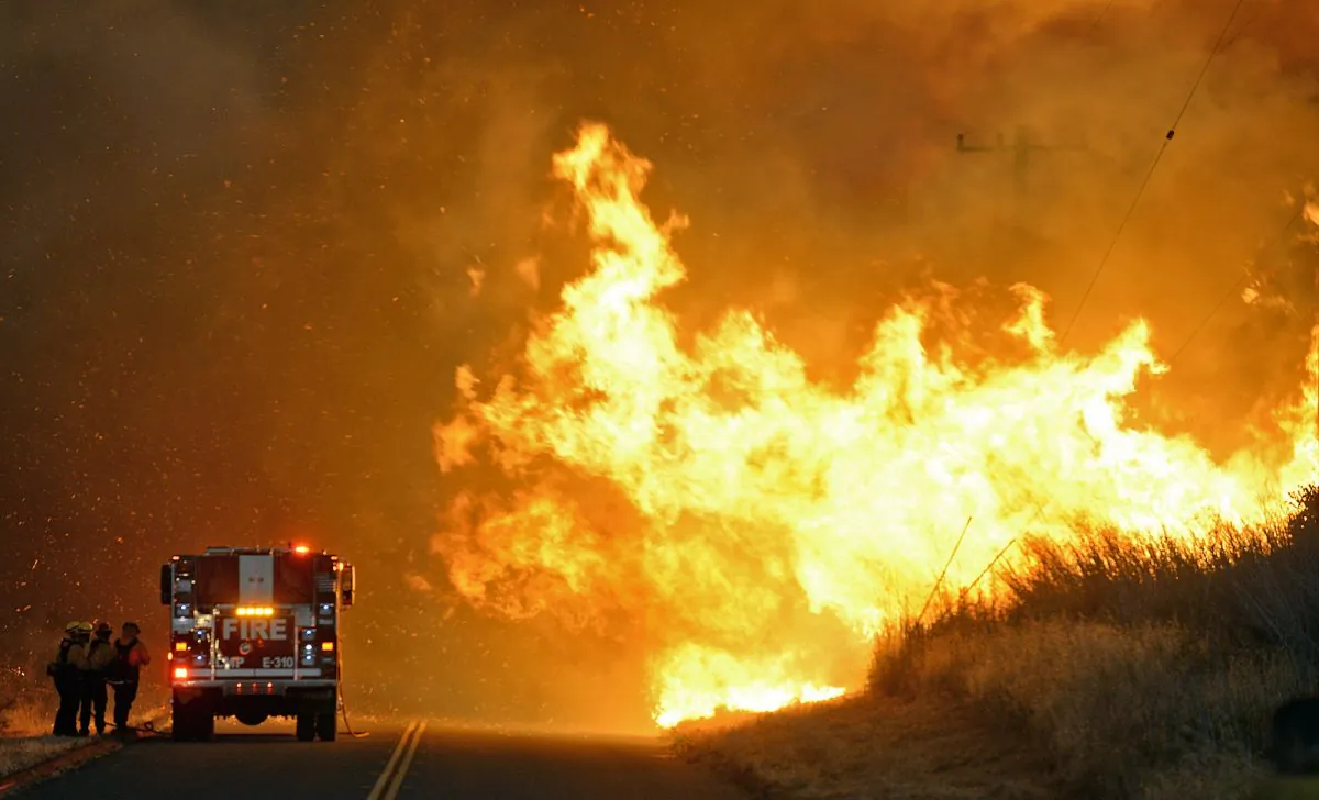 Firefighters from the Lompoc City Fire Department take shelter behind their engine on June 16, 2016, as wind driven flames advance from the Sherpa Fire. The flames were crossing Calle Real near El Capitan State Park in Santa Barbara County. (Mike Eliason/Santa Barbara County Fire Department via AP)